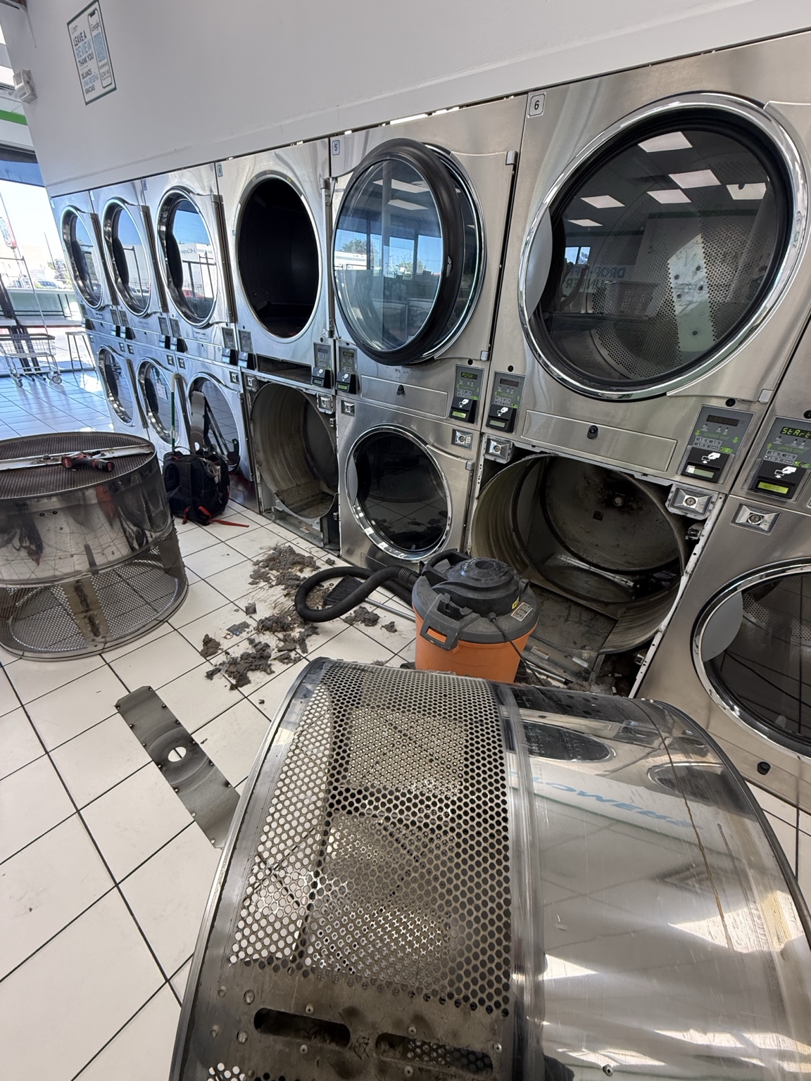 Stack dryers during service with drums removed, tools, and a shop vacuum beside the machines